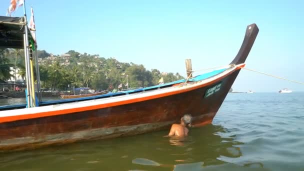 Рыбак чистит корму своей старой лодки рано утром в Таиланде — стоковое видео