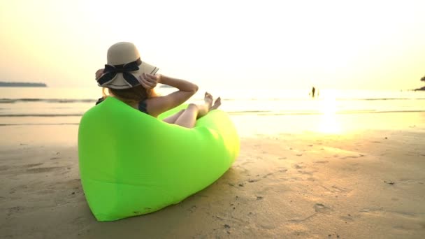 Een jonge vrouw met een strohoed die geniet van rust en privacy bij zonsondergang op het strand — Stockvideo