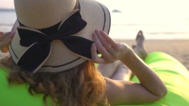 Hasır şapkalı genç bir kadın kumsalda gün batımında huzur ve mahremiyetin tadını çıkarıyor.