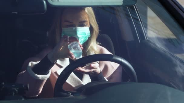 Mujer joven en máscara médica estéril protectora utiliza líquido desinfectante de manos en un coche — Vídeos de Stock