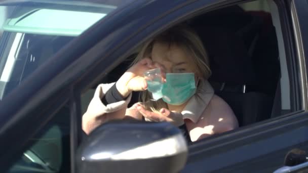Jeune femme dans un masque médical stérile protecteur utilise un liquide désinfectant pour les mains dans une voiture — Video
