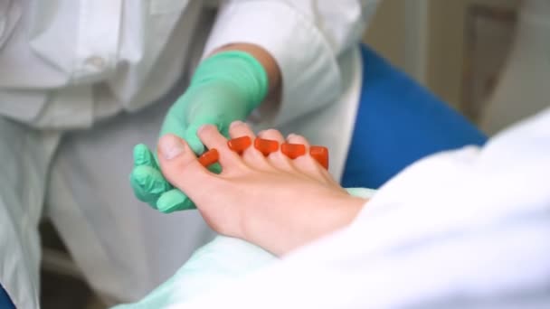 Um pedicurista enverniza uma jovem mulher unhas dos pés — Vídeo de Stock