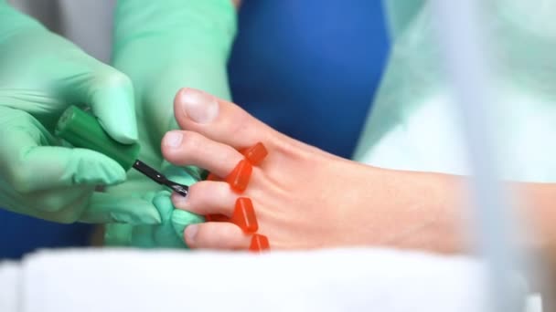 Um pedicurista enverniza uma jovem mulher unhas dos pés — Vídeo de Stock