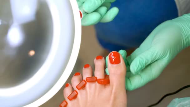 Um pedicurista enverniza uma jovem mulher unhas dos pés — Vídeo de Stock