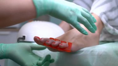 Bir pedikür uzmanı genç bir kadının tırnaklarını cilalar.