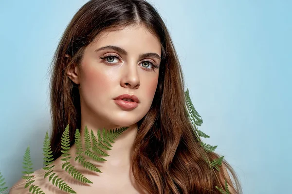 Retrato de una mujer morena adulta sobre fondo azul con helecho verde — Foto de Stock