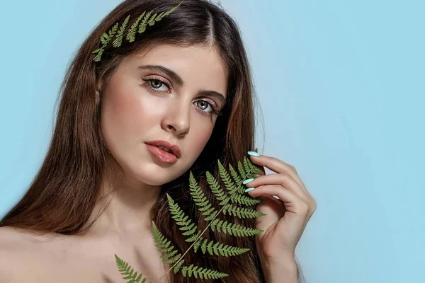 Portrait of an adult brunette woman on a blue background with green fern — 스톡 사진