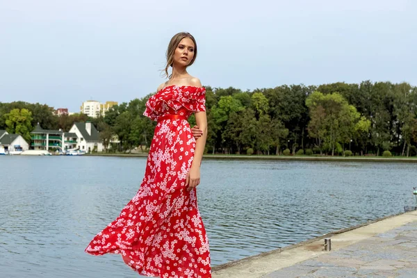 Retrato de uma bela jovem menina de cabelos castanhos com cabelos longos em um vestido vermelho em um fundo do lago . — Fotografia de Stock