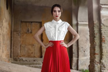 Eski, terk edilmiş bir binanın arka planında kahverengi saçlı, şık kırmızı etekli ve gömlekli güzellik mankeni kız. Mükemmel makyajlı ve moda elbiseli seksi bir kadın portresi..