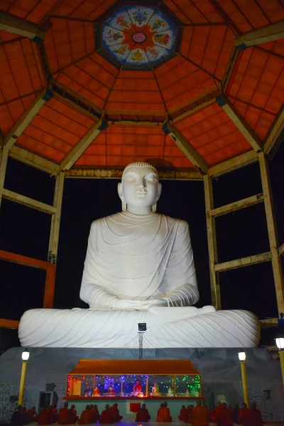 Vista nocturna de la estatua de Buda con monjes sentados y rezando . — Foto de Stock