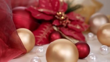 Altın ve kırmızı tonlarda Noel kompozisyonu Poinsettia çiçeği ve takılar. 4K çözünürlüklü doli çekimi.