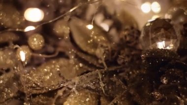 Karanlıkta küçük ışıklarla parlayan altın Noel çelengi. 4K çözünürlük, makro, dolly shot. Sığ alan derinliği.