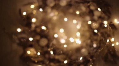 Karanlıkta küçük ışıklarla parlayan altın Noel çelengi. 4K çözünürlüklü bebek atışı. Üst Manzara. Sığ alan derinliği.