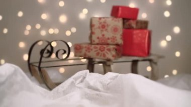 Beyaz kar üzerinde hediyeli bir Noel kızağı. Arka planda sönmüş ışıklar var. 4K çözünürlüklü bebek atışı. Sığ alan derinliği.