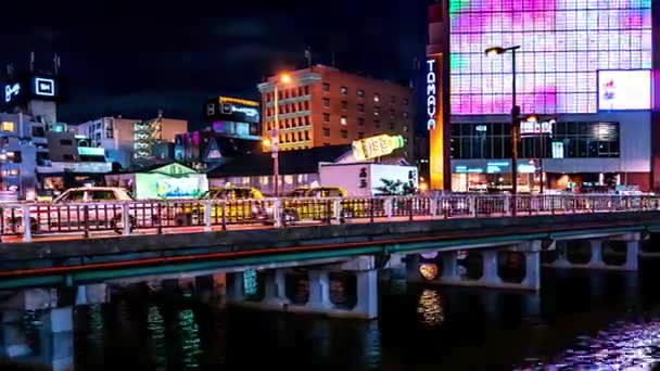 福岡-橋の上のトラフィックとカラフルな輝く画面で川で輝く街の夜景。4K解像度のタイムラプスパン. — ストック動画