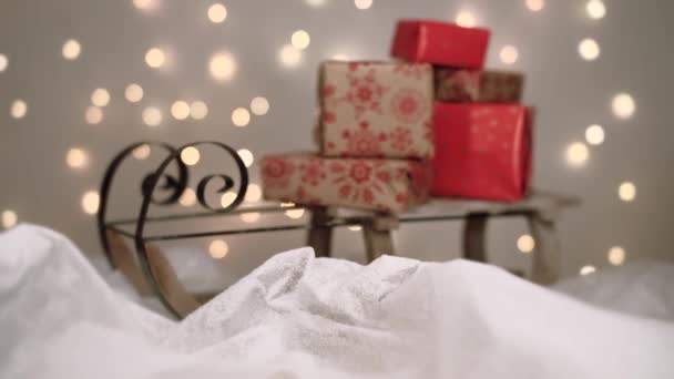 Beyaz kar üzerinde hediyeli bir Noel kızağı. Arka planda sönmüş ışıklar var. 4K çözünürlüklü bebek atışı. Sığ alan derinliği. — Stok video