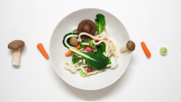 Verduras y fideos udon convirtiéndose en una sopa. Los ingredientes frescos entran en el plato y luego se cocinan. Detener la animación en movimiento sobre fondo blanco. Resolución 4K — Vídeos de Stock