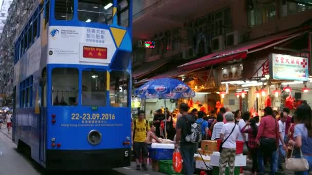 HONG KONG - Wieczorny widok mokrego rynku z ludźmi i dwupiętrowy tramwaj przejeżdżający obok. Rozdzielczość 4K. — Wideo stockowe