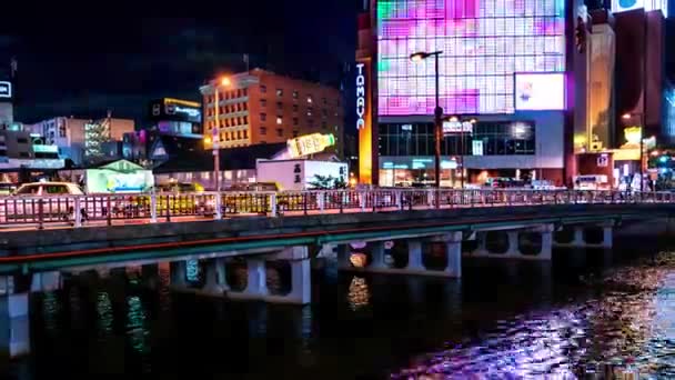 Fukuoka - Vista nocturna de la ciudad brillante junto al río con el tráfico en el puente y la pantalla brillante de colores. Resolución 4K time lapse zoom out . — Vídeos de Stock