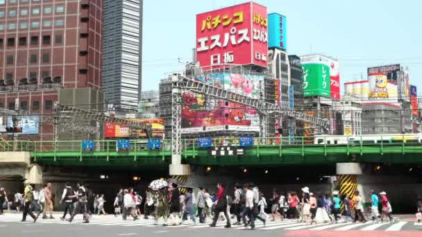 Tokyo, Japan - Människor på gatukorsning med färgglada skyltar i bakgrunden, tåg och bilar passerar. Det är Shinjuku. 4K-upplösning — Stockvideo