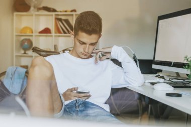 genç ya da genç adam öğrenci üstünde okul sırası ile cep telefonu ve bilgisayar