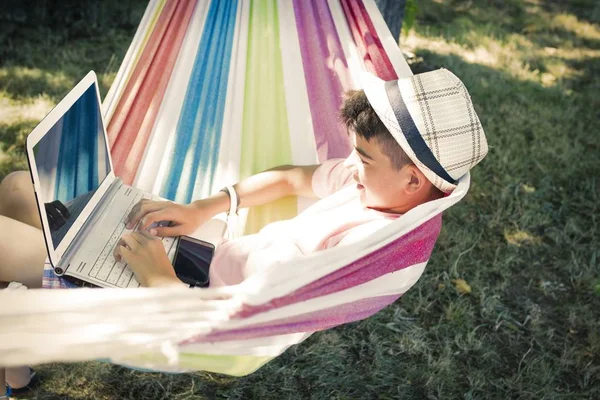 勉強で遊んだり 夏の夕暮れ時にハンモックでラップトップを持つ子供 — ストック写真