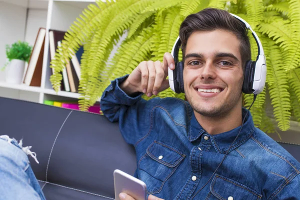Νεαρός Άνδρας Στο Σπίτι Lounge Τηλέφωνο Και Ακουστικά Ακούτε Μουσική — Φωτογραφία Αρχείου