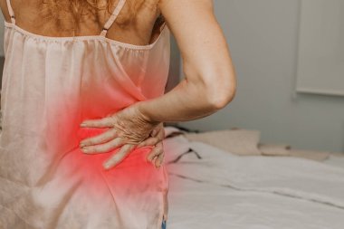 Yatak odasında kas ağrısı belirtileri gösteren yetişkin bir kadın var.