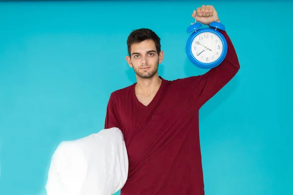 young man with pajamas and alarm clock with pillow isolated on color background