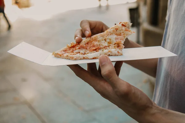 hands with slice of pizza on urban street outdoors