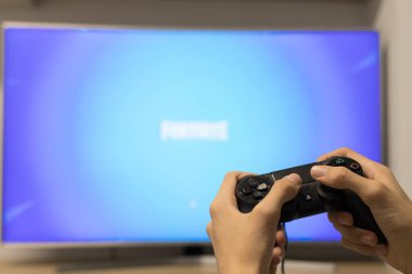 Galiçya, İspanya - 29 Eylül 2019: Playstation kontrolörü olan bir çocuğun elleri televizyonda Fortnite ile oynuyor