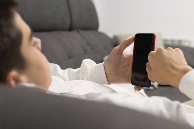 Kanepede cep telefonu olan genç bir adam.