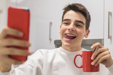 Genç adam evde kahve fincanıyla cep telefonuyla fotoğraf çekiyor.