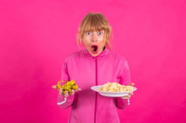 woman with stress expression looking at measuring tape and plate of pasta or hydrates with sportswear isolated on pink background