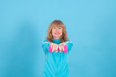 woman with expression of effort or tiredness with exercise dumbbells isolated on blue background clipart