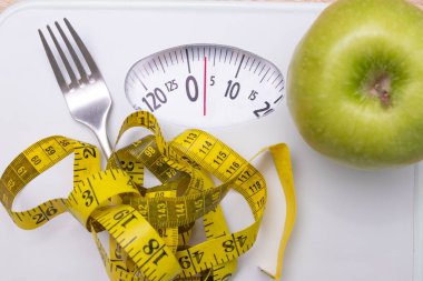 scale with measuring tape and fork with apple, diet concept