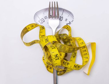 closeup of scale with measuring tape and fork, concept of diet and losing weight