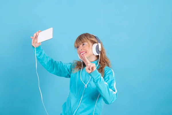Ενήλικη Γυναίκα Κινητό Τηλέφωνο Και Ακουστικά Κάνοντας Selfie Απομονωμένη Μπλε — Φωτογραφία Αρχείου