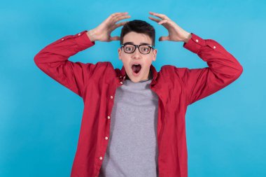 Genç bir adam ya da genç bir öğrenci. Renkli arka planda izole edilmiş. Elleri başının üstünde, şaşkınlık içinde.