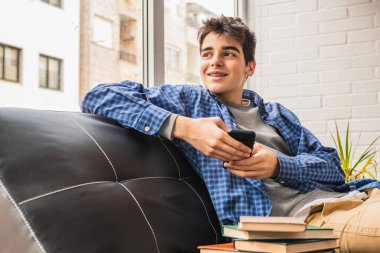 Genç bir çocuk cep telefonuyla kanepede oturuyor.