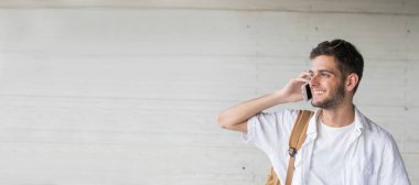 Dışarıda cep telefonuyla konuşan gülümseyen öğrenci ya da genç adamın portresi.