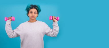 Kadın aerobik yaparken arka planda izole edilmiş aerobik ağırlıkları kullanıyor.