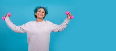 Kadın aerobik yaparken arka planda izole edilmiş aerobik ağırlıkları kullanıyor.