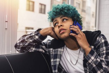 Genç bir kadın ya da kız cep telefonu evde ya da dairesinde mavi saçlı Afro-Amerikan kıvırcık saçlı.