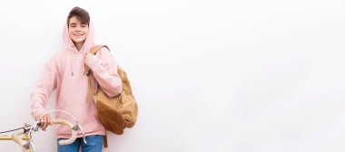 Beyaz duvara izole edilmiş sırt çantası ve bisikleti olan genç öğrenci ya da çocuk.