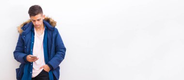 Akıllı telefonlu genç adam sokak duvarına yaslanıyor.