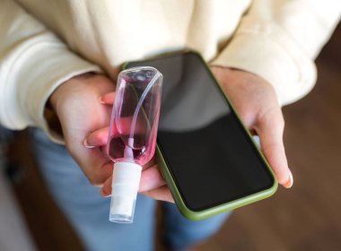 Kız telefonu kirden, virüsten ve dezenfeksiyondan aldığı antiseptikle siler.