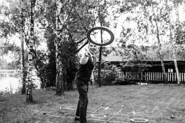 black and white photo, a young guy in an official suit plays a game, throws a circle on the lawn