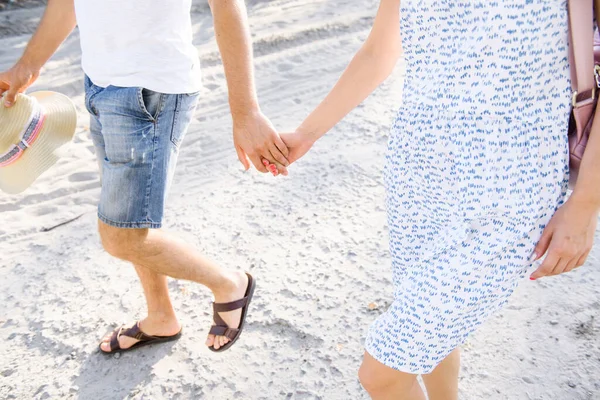 young couple in summer clothes walk on the sand holding hand