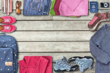 Yukarıdan görünüm in unisex seyahat gerekli bir sırt çantası, Ayakkabı, Giysi, bir dijital fotoğraf makinesi, güneş gözlüğü, kozmetik çantası ve bir pasaport (ABD), gibi bir çerçeve ahşap zemin üzerinde bir şekil düzenlenmektedir